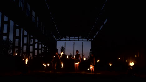 Eine-Gruppe-Von-Menschen-Mit-Feuer-Und-Fackeln-Tanzt-Bei-Sonnenuntergang-Im-Hangar-In-Zeitlupe.-Feuershow.